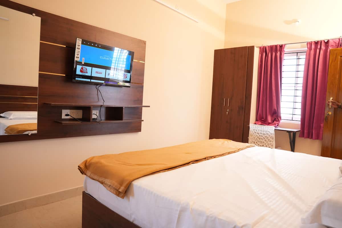 Une chambre d’hôtel avec un lit, un téléviseur fixé au mur, une armoire et une fenêtre avec des rideaux.
