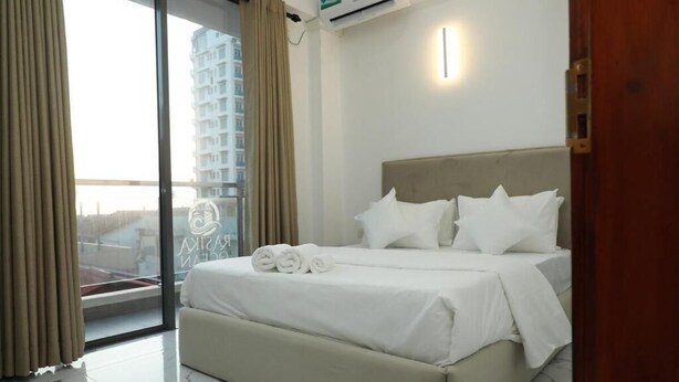 Habitació d'hotel amb un llit, una finestra amb cortines, un aparell d'aire condicionat i vista a un edifici.
