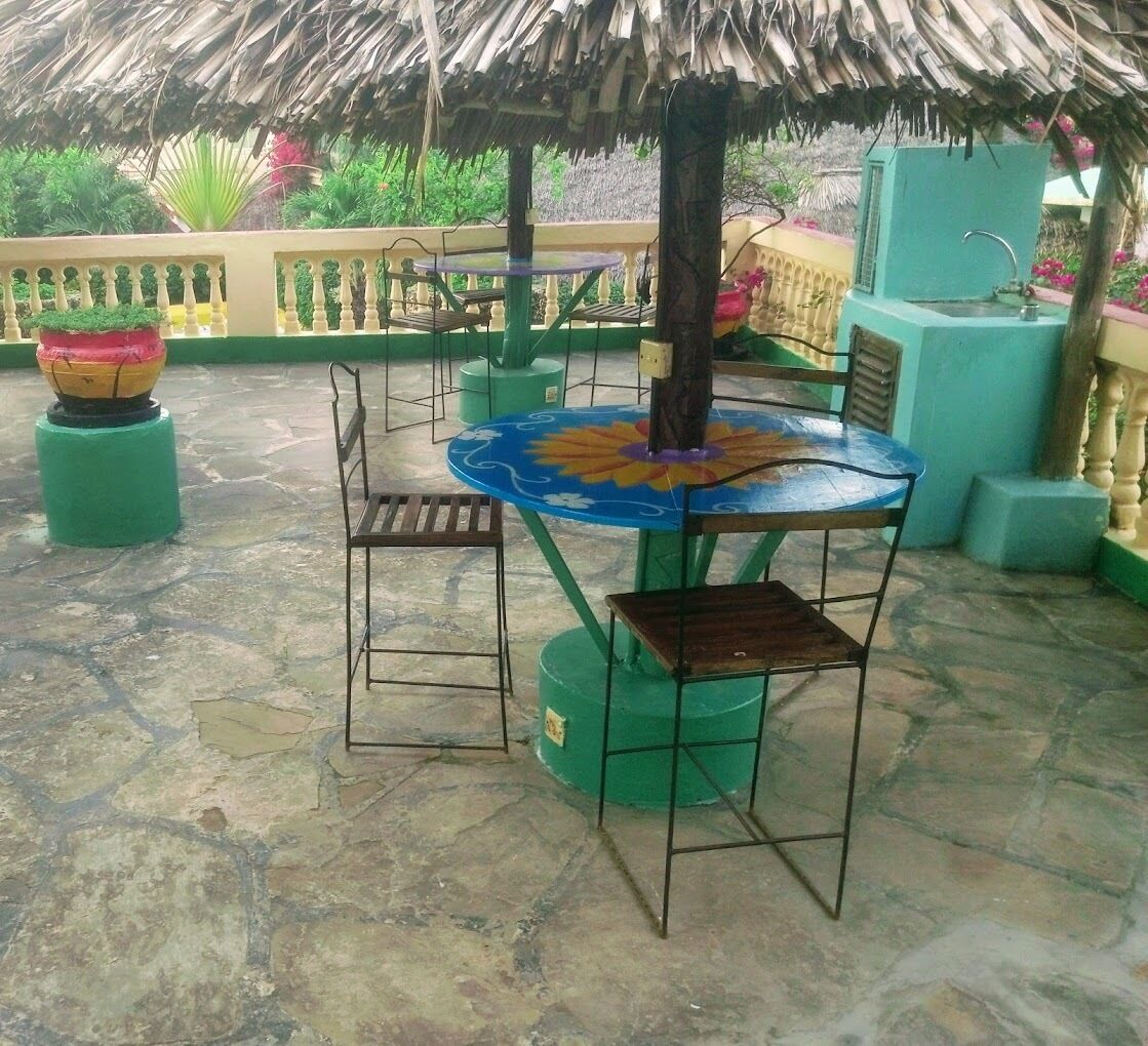Une terrasse extérieure avec une table ronde et deux chaises, un toit de chaume et un motif floral décoratif sur la table.