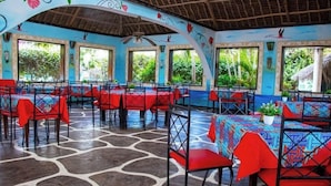 A restaurant with red chairs and tables, large windows, and a tropical mural on the walls. - Malindi Breeze Point Hotel (Malindi)