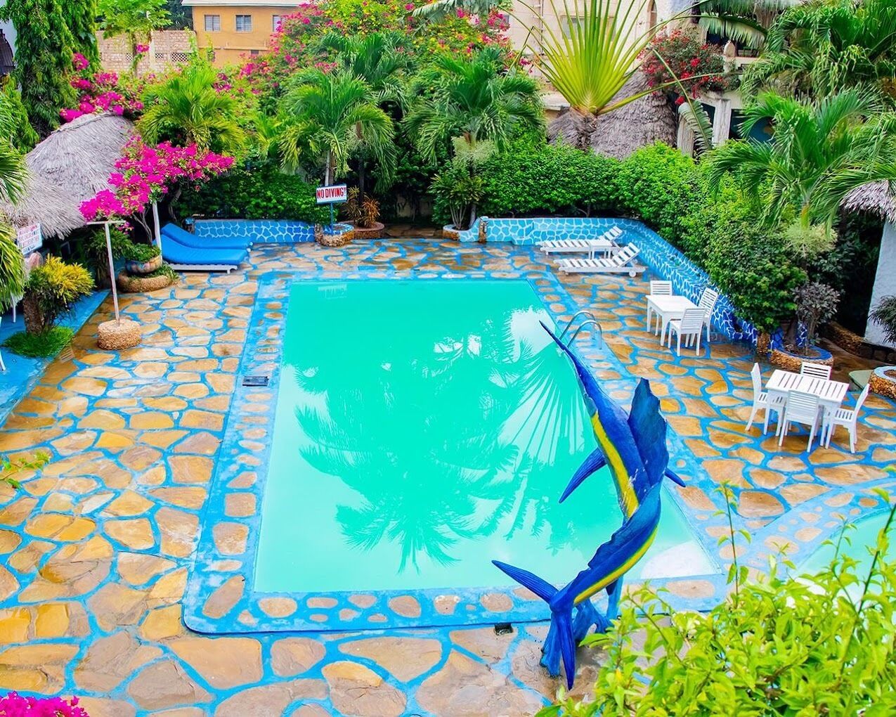 Un área de piscina con suelo de piedra, sillas de descanso y plantas tropicales.
