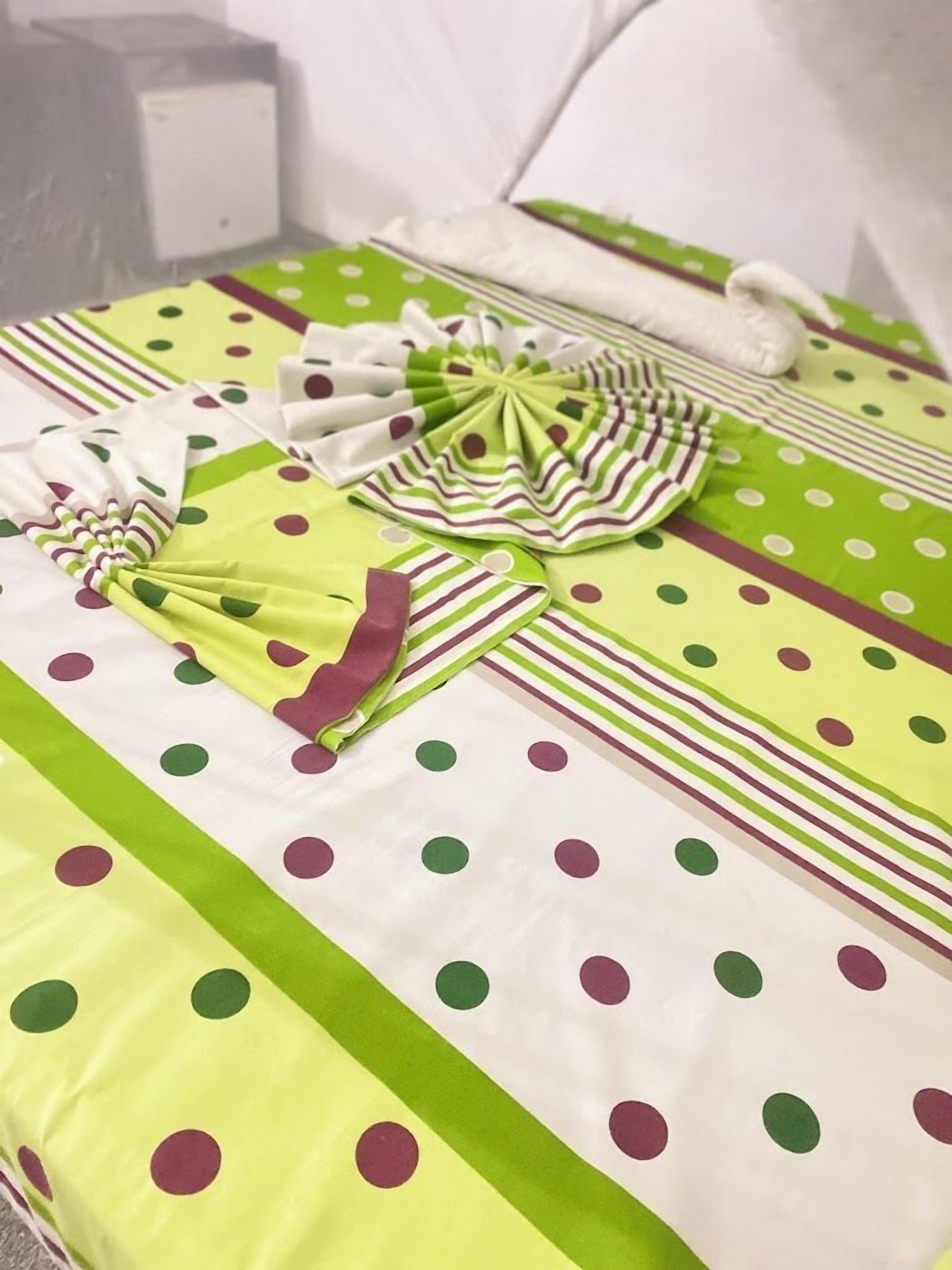 A neatly made bed with a polka dot and striped bedspread, a folded green and white striped pillow, and a matching pillow on the bed.