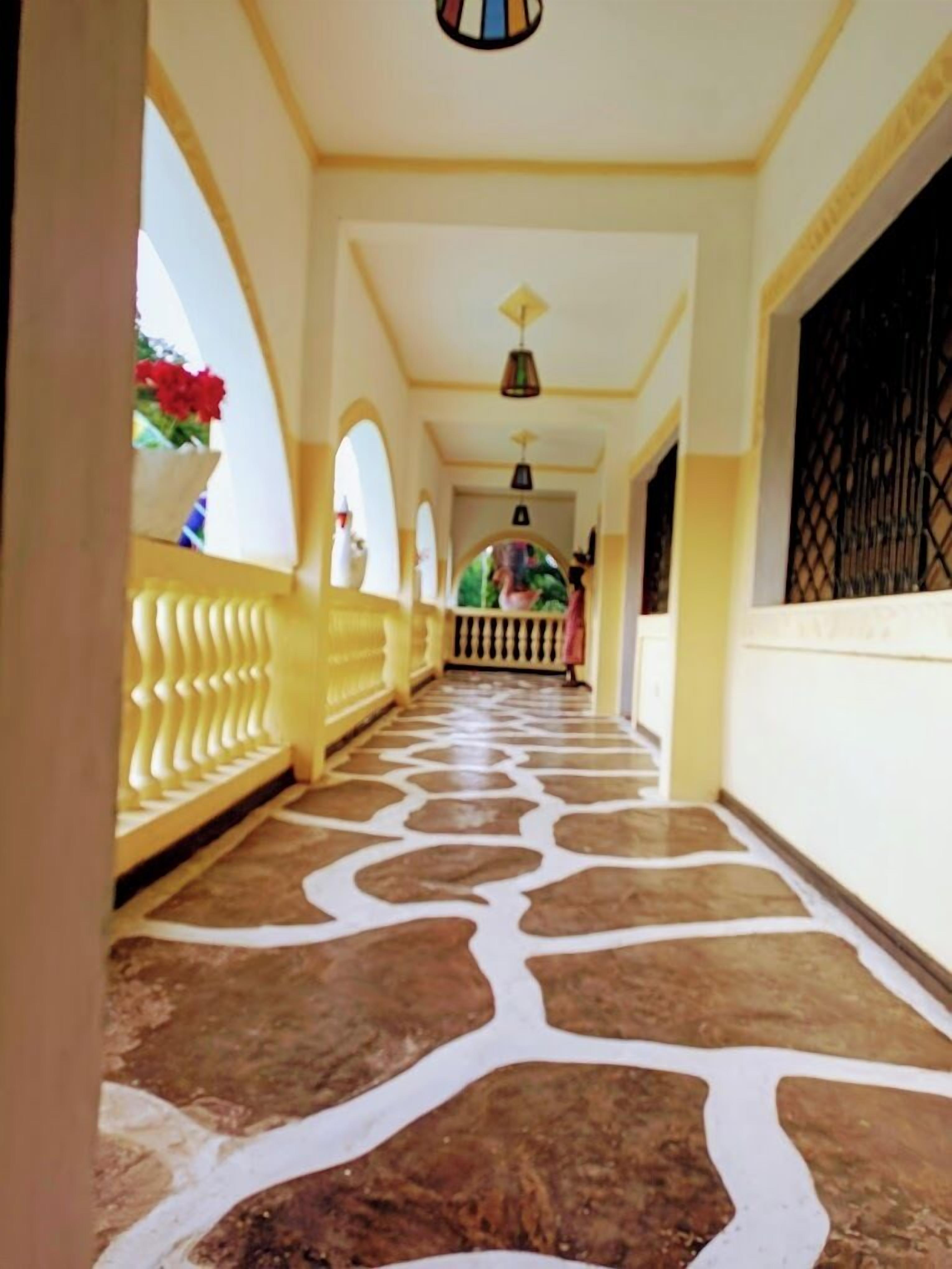 A corridor with a patterned floor, yellow walls, and a railing on one side.