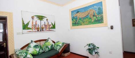 A room with a wooden sofa, a ceiling fan, and two framed paintings on the walls.