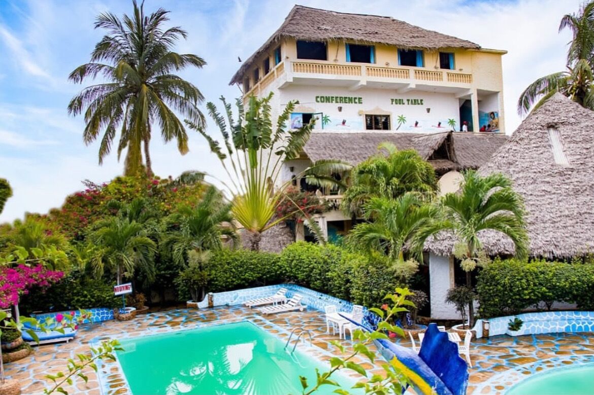 A hotel with a pool area, palm trees, and a thatched-roof building labeled "CONFERENCE POOL TABLE".