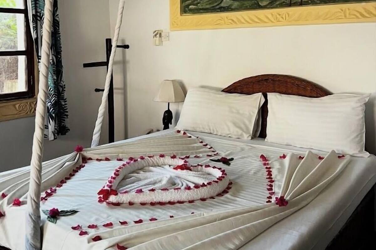 A bed with a canopy, a painting of swans, and a nightstand with a lamp.