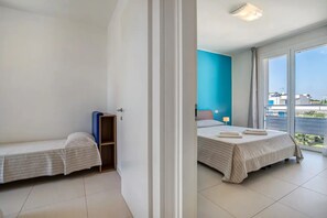 Ein Hotelzimmer mit zwei Betten, einem kleinen Holzschrank, einem großen Fenster mit Blick und einer Deckenleuchte.