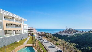 Un hotel moderno con piscina, vistas al mar y un paisaje montañoso al fondo.