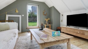 A cozy room with a bed, a wooden table, a TV, and a window with a view of greenery. - Charming Townhouse in St Renan (Saint-Renan)