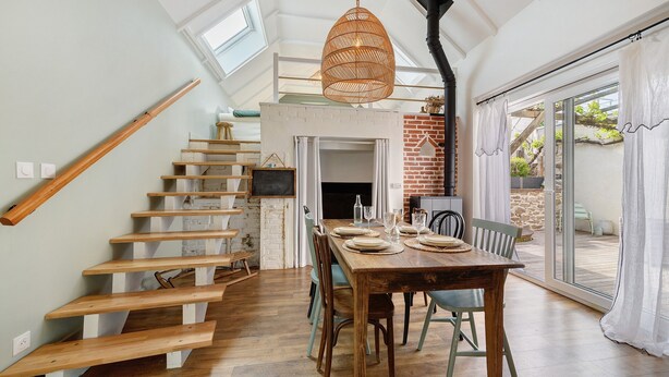 A dining area with a wooden table, chairs, and a staircase leading to an upper level. - Charming Townhouse in St Renan (Saint-Renan)