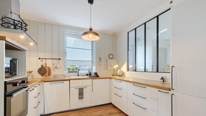 A modern kitchen with white cabinetry, a wooden countertop, a hanging light fixture, and a large window. - Charming Townhouse in St Renan (Saint-Renan)
