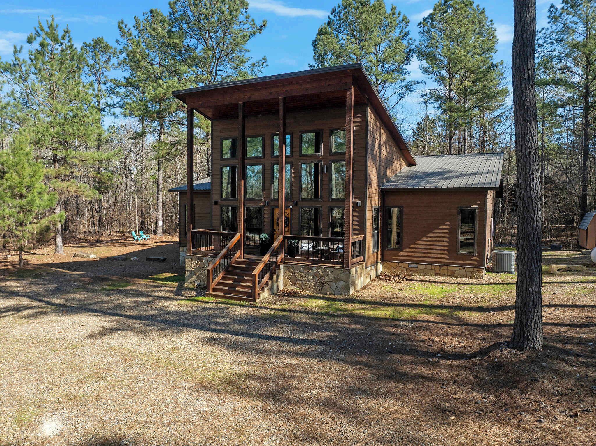 A cabin with a wooden exterior, large windows, and a porch with stairs.