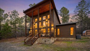 A two-story log cabin with a stone foundation, a wooden deck, and a staircase leading to the upper level. - Hoot's Hideaway w/ Hot Tub (Broken Bow)