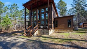 A two-story log cabin with a stone foundation, large windows, and a wooden staircase leading to the upper level. - Hoot's Hideaway w/ Hot Tub (Broken Bow)