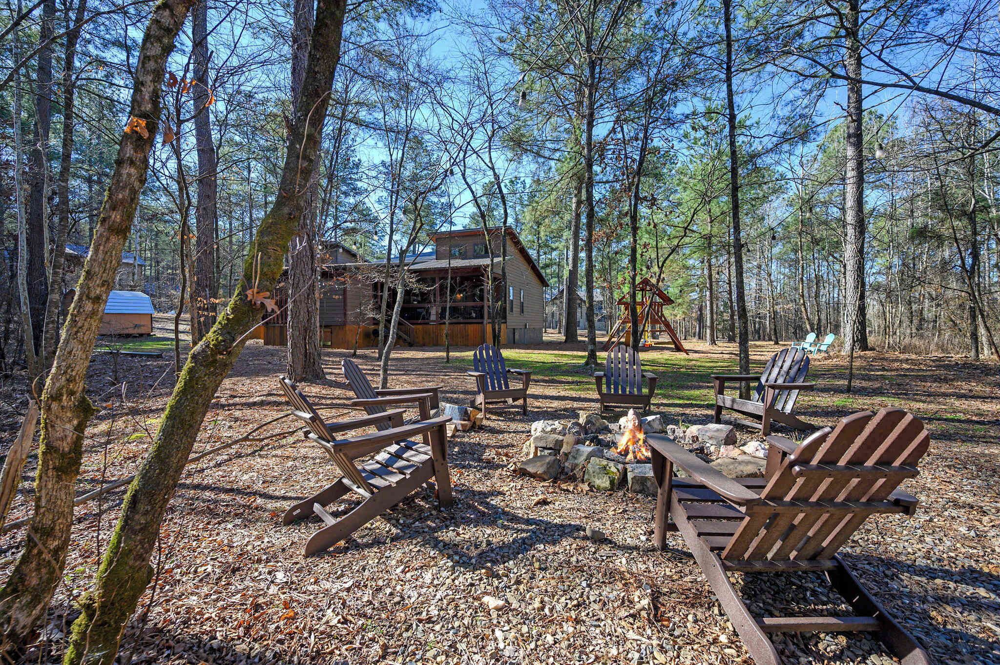 A cabin with a fire pit and Adirondack chairs in a forest setting.
