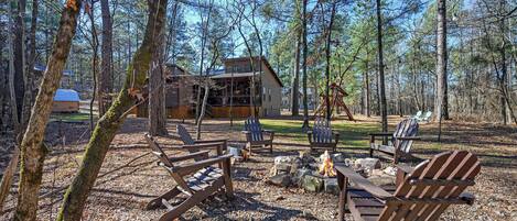 A cabin with a fire pit and Adirondack chairs in a forest setting.