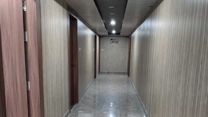 A corridor with tiled flooring and wooden doors, leading to a room with a ceiling light. - Hotel The Royal Knot (Kanpur)