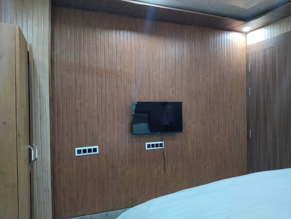 A room with wooden panel walls, a mounted TV, and a bed. - Hotel The Royal Knot (Kanpur)