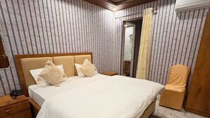 A bedroom with a large bed, wooden headboard, and a ceiling fan. - Hotel The Royal Knot (Kanpur)
