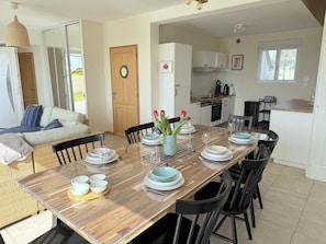 A dining area with a wooden table set for six, surrounded by black chairs. A kitchen is visible in the background with white cabinets and a window. - Panoramic sea View - Le Conquet (Le Conquet)