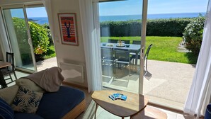 A room with a sofa, a small table, and a view of the sea through a glass door. - Panoramic sea View - Le Conquet (Le Conquet)