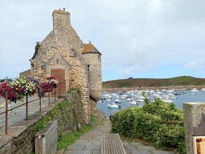 A stone building with a wooden door, surrounded by a stone wall and steps leading down to a harbor with boats. - Panoramic sea View - Le Conquet (Le Conquet)