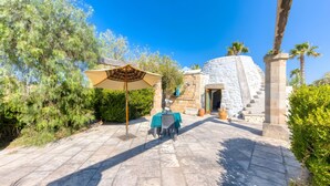 Eine Terrasse mit Tisch und Sonnenschirm, Steinmauern und Palmen.