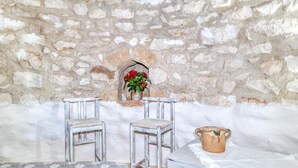 Eine rustikale Steinmauer mit kleinem Durchgang, zwei Holzstühle, ein Tisch und eine Vase mit Blumen.