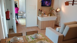 En moderne stue med en sofa, et spisebord dækket med tallerkener og kopper, et tekøkken med et fjernsyn og en brandslukker.