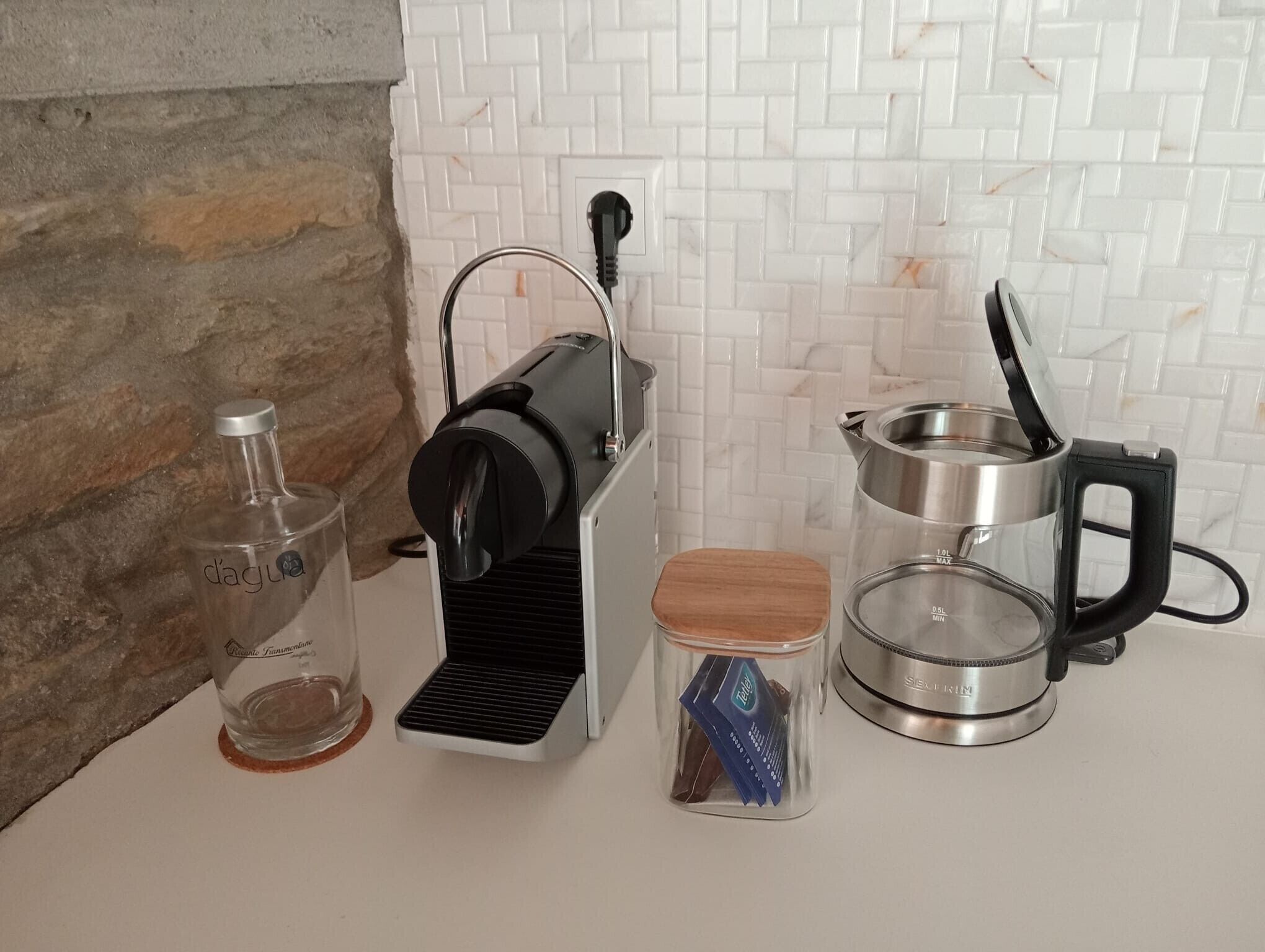Et køkken med kaffemaskine, et glas og en elkedel.