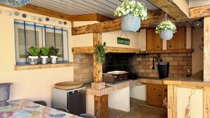 A rustic kitchen with a brick wall, wooden beams, a stove, and hanging planters. - Fully equipped pool house Canet plage perfect for a nice vacation (Canet-en-Roussillon)
