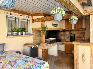 A rustic kitchen with a brick wall, wooden beams, a stove, and hanging planters.