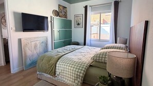 A bedroom with a bed, a TV, a bedside lamp, a window with curtains, and a green wall. - Fully equipped pool house Canet plage perfect for a nice vacation (Canet-en-Roussillon)