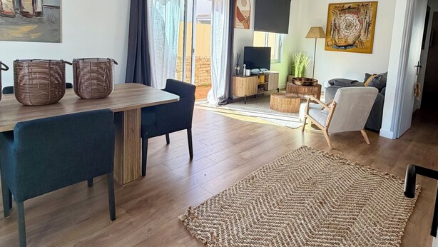 A spacious living area with a wooden dining table, blue upholstered chairs, a woven rug, and a flat-screen TV mounted on the wall. - Fully equipped pool house Canet plage perfect for a nice vacation (Canet-en-Roussillon)