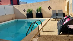 A swimming pool with a metal ladder, two lounge chairs, and potted plants against a wall. - Fully equipped pool house Canet plage perfect for a nice vacation (Canet-en-Roussillon)