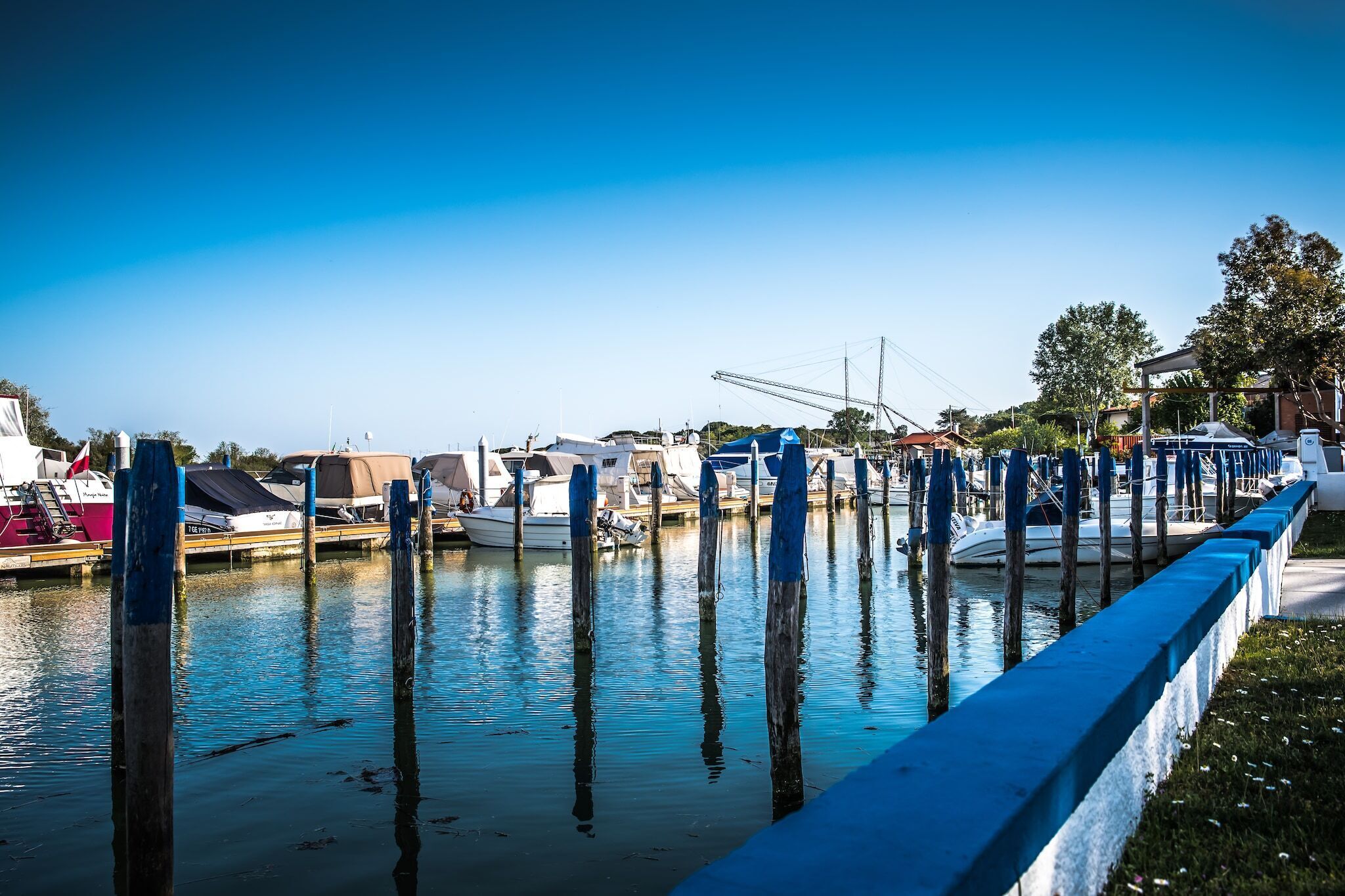 Un port de plaisance avec des bateaux amarrés, des poteaux en bois et un ciel bleu azur.