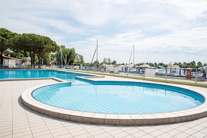 A swimming pool with a tiled deck, surrounded by a fence and trees. - Bungalow im Marina di Cortellazzo Jesolo (Cortellazzo Jesolo)