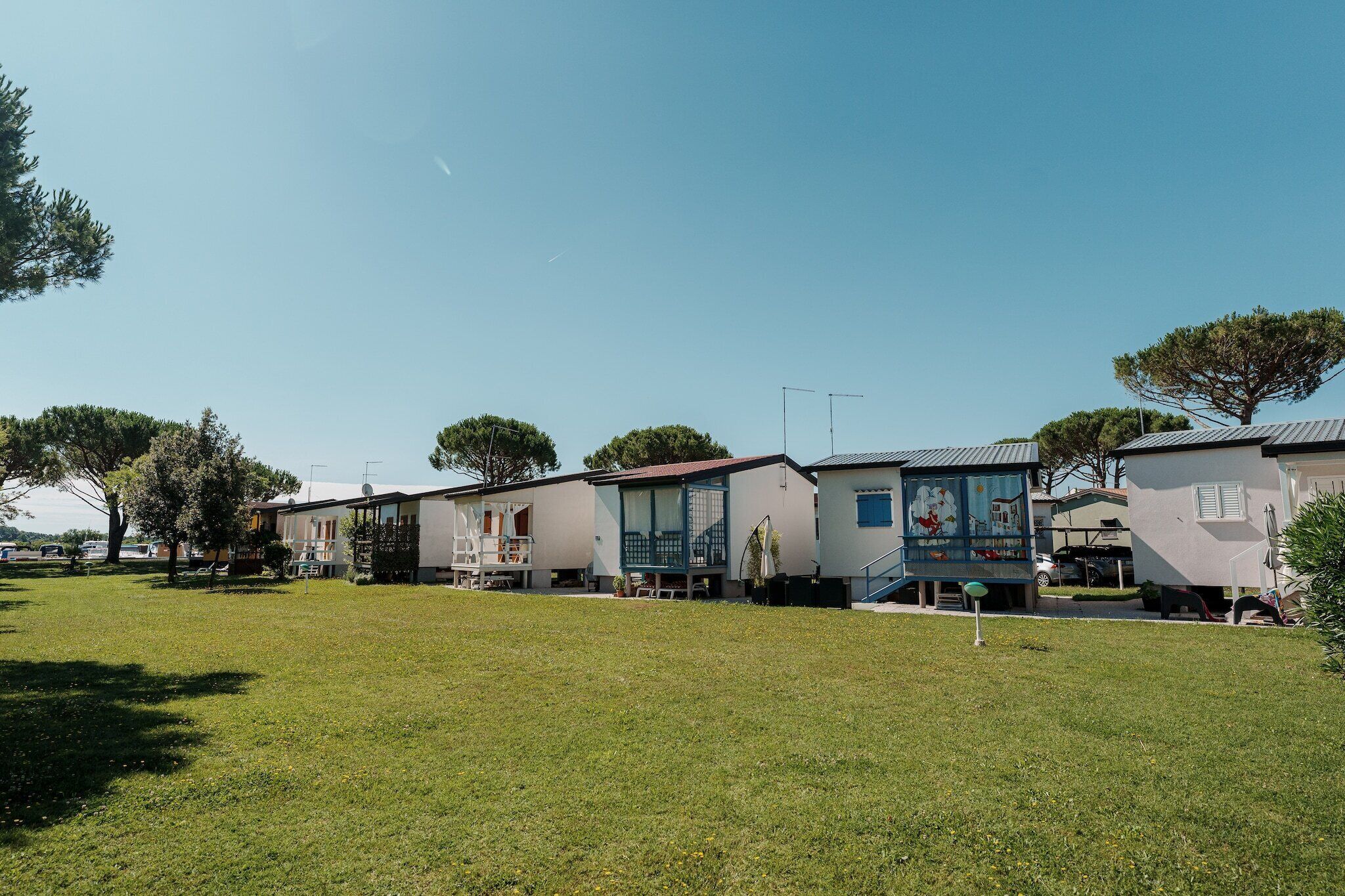 Une rangée de maisons de plain-pied, chacune dotée d’une petite véranda et d’une fenêtre, et devant laquelle s’étend une pelouse verdoyante.