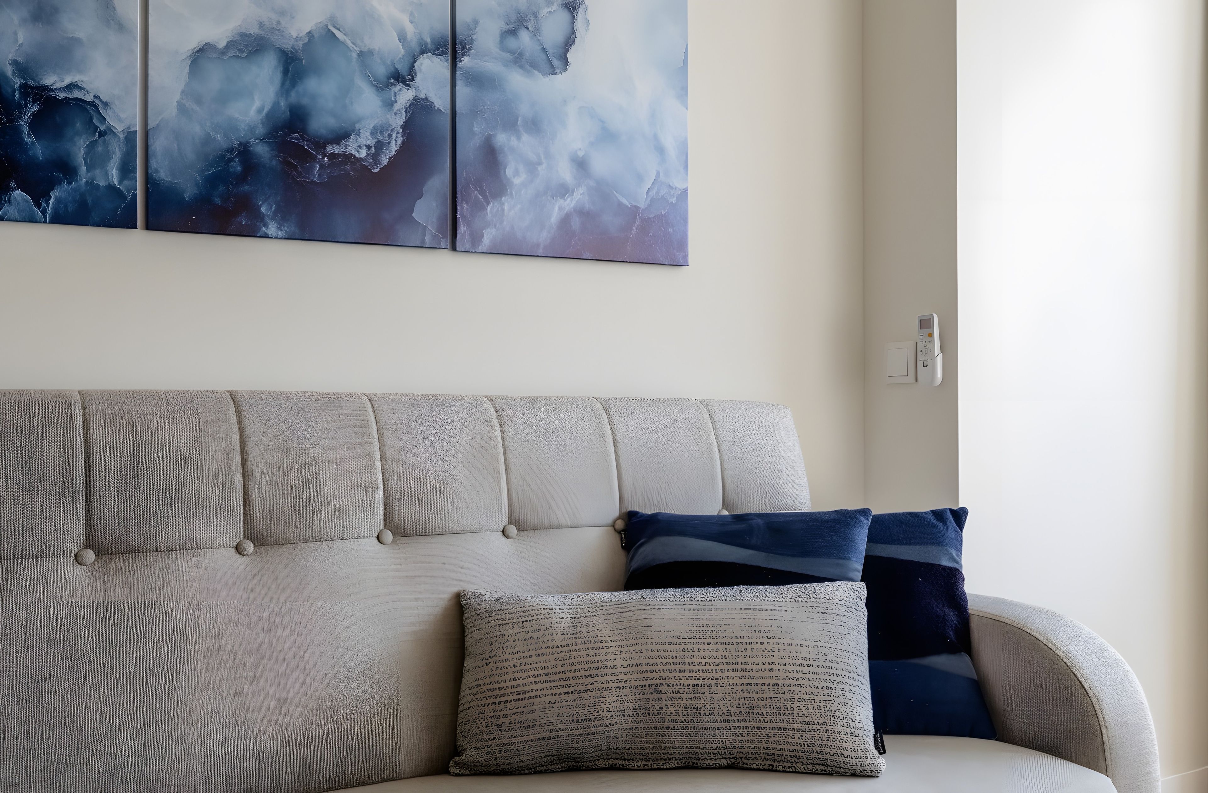 A living room with a sofa, two pillows, and a wall-mounted thermostat.