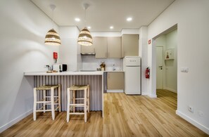Une cuisine moderne dotée d’un îlot central, de deux tabourets de bar, de luminaires suspendus et d’un réfrigérateur.