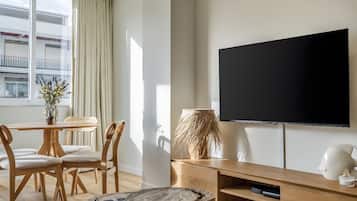 Una sala de estar moderna con un televisor de pantalla plana, muebles de madera y vistas a un edificio a través del ventanal.