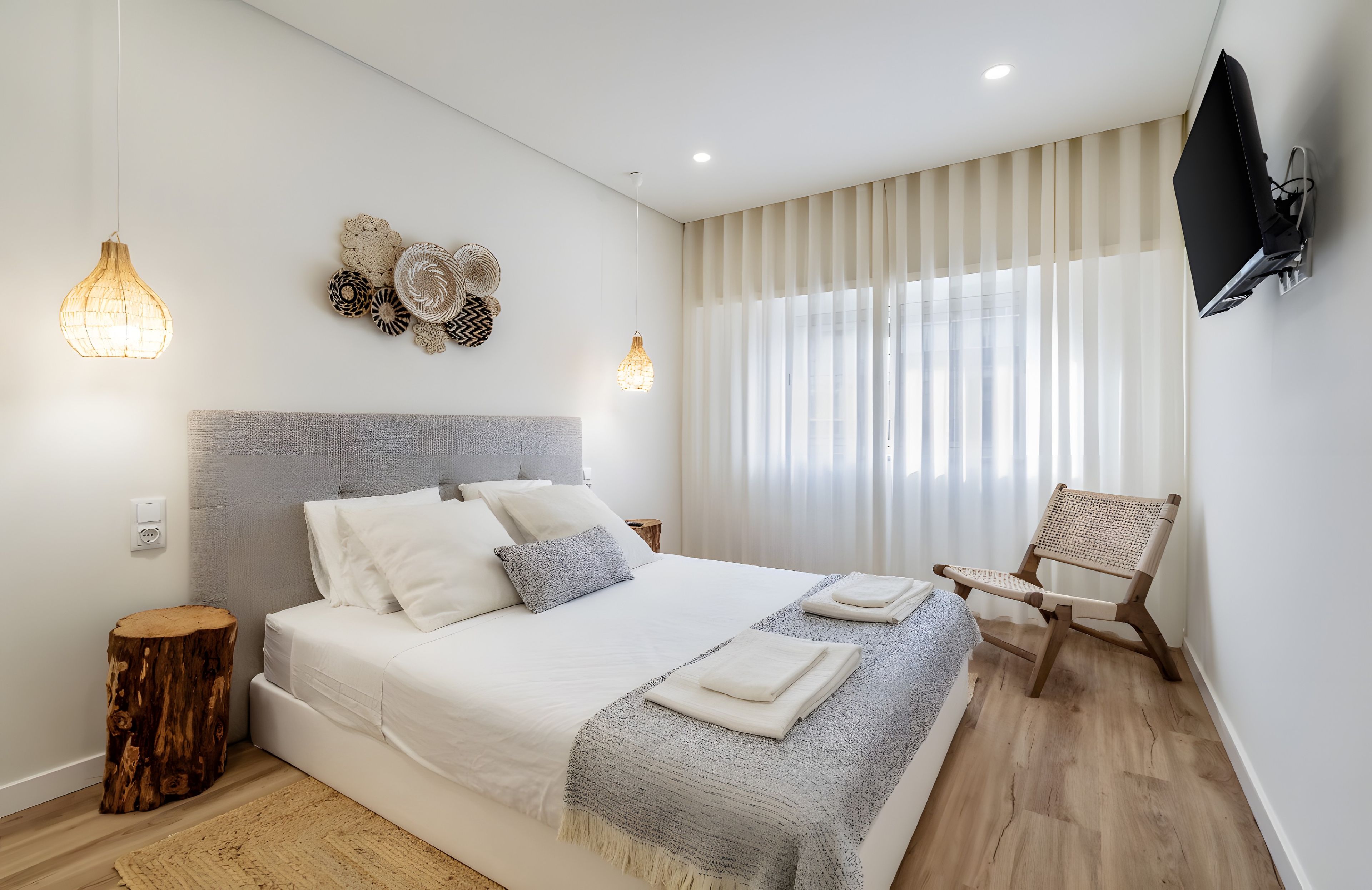 A modern bedroom with a large bed, a mounted TV, and a wooden chair.