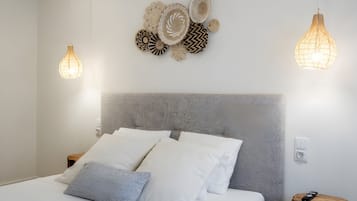 Una cama impecablemente tendida con ropa de cama blanca y gris, un cabecero texturizado y una lámpara fijada a la pared.