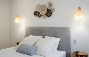 Un lit bien fait, avec une literie blanche et grise, une tête de lit texturée et un luminaire fixé au mur.