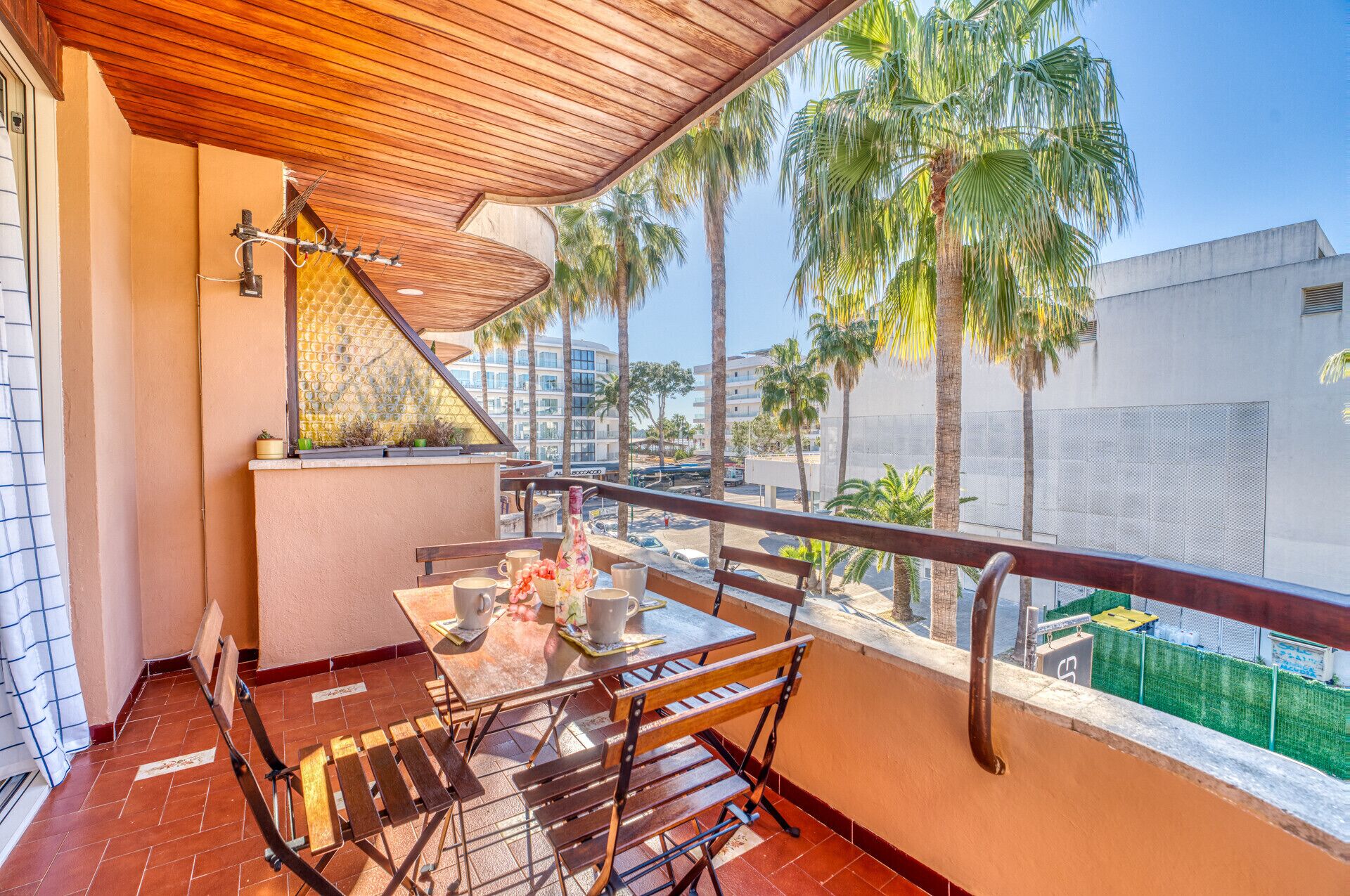 Un balcon doté d’un plafond en bois, d’une table avec des chaises et d’une vue sur des palmiers et des immeubles.