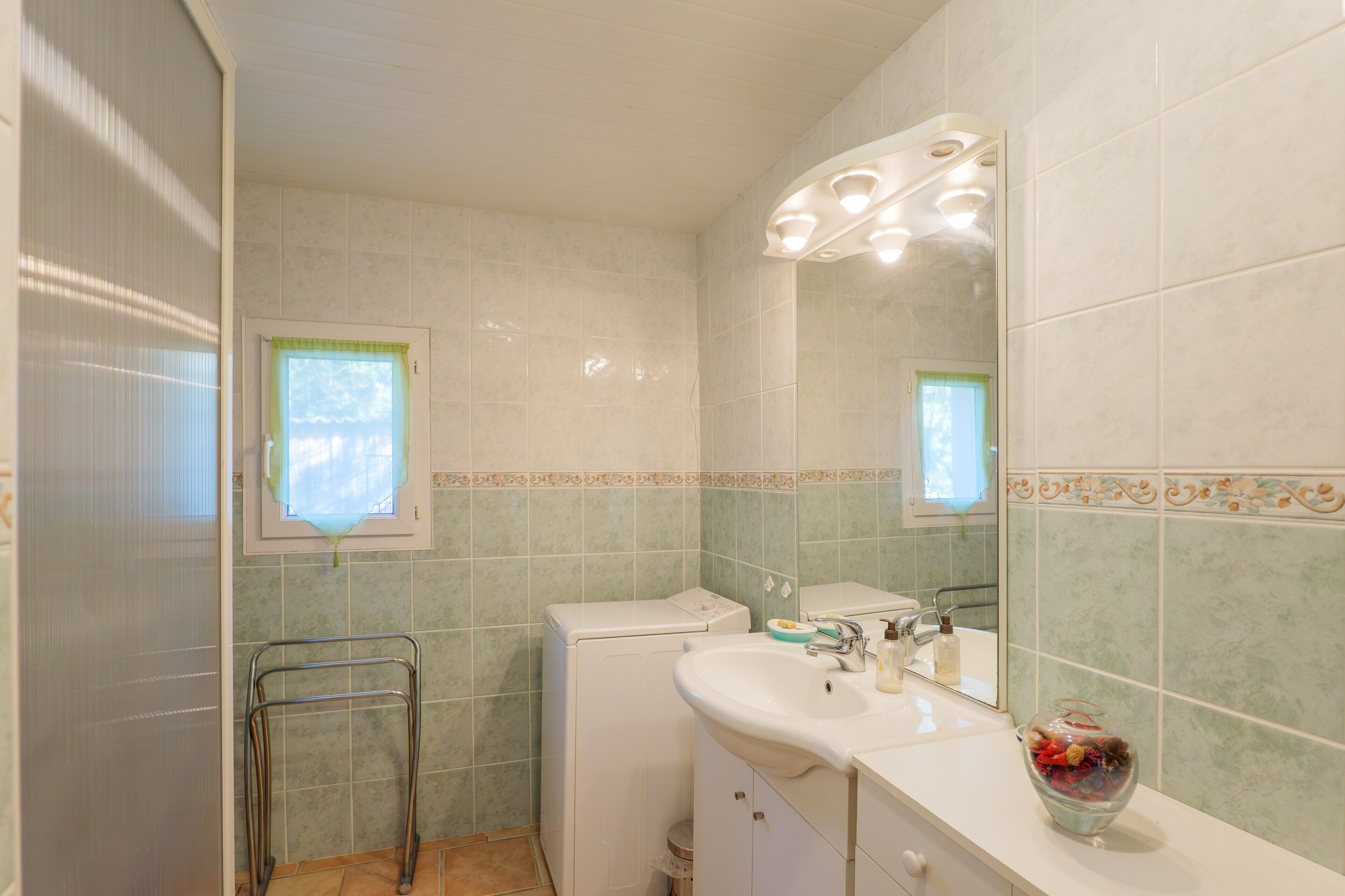 A bathroom with a white sink, a glass vase, and a mirror.