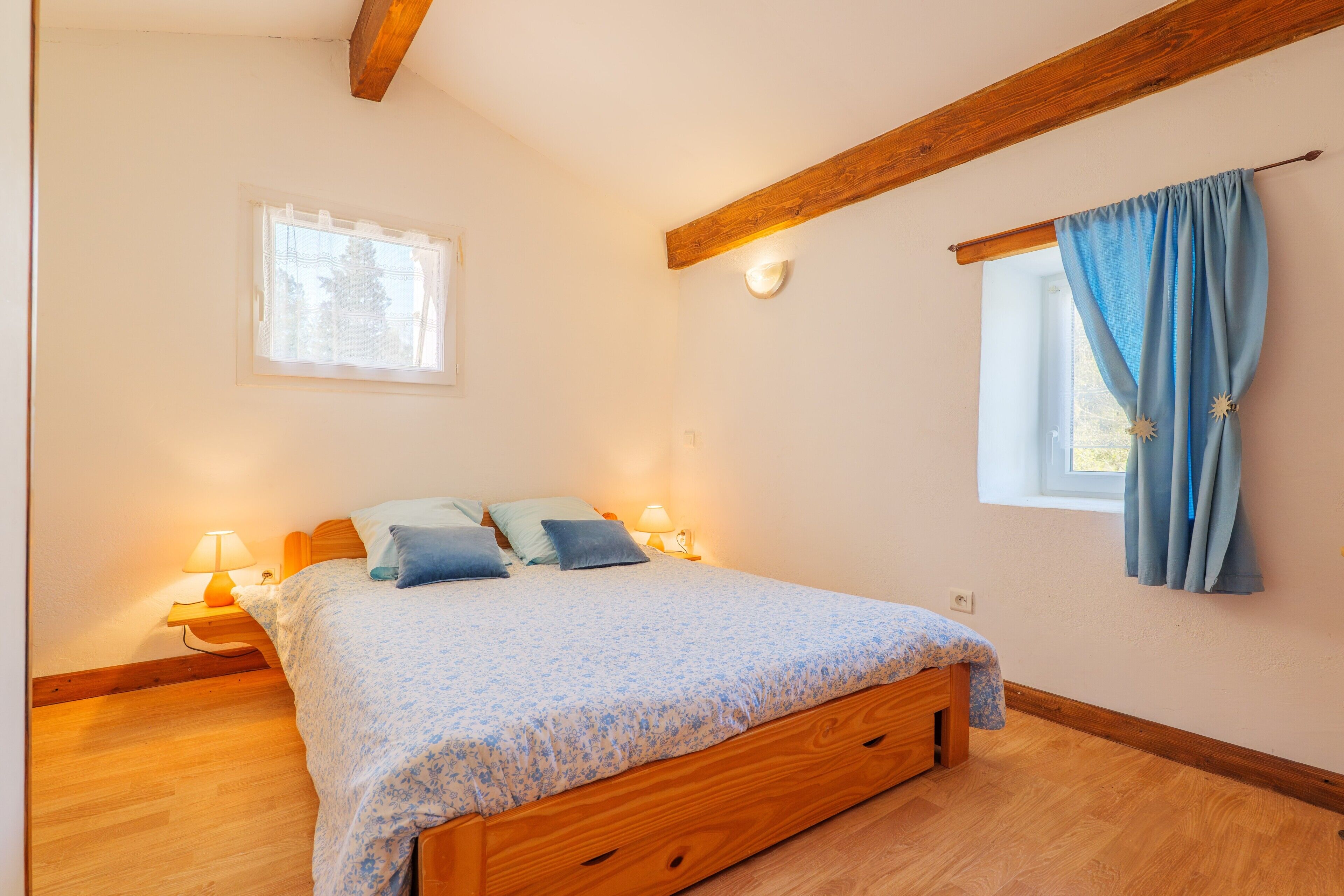Ein Schlafzimmer mit einem hölzernen Bett, zwei Nachttischlampen, einem Fenster mit Vorhängen und einem kleinen Fenster über dem Bett.