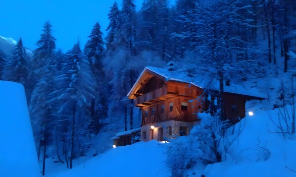 Eine Holzhütte mit einem Balkon, umgeben von schneebedeckten Bäumen.