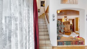 Escada que leva a um quarto com estantes de livros, uma planta e um banco de madeira.