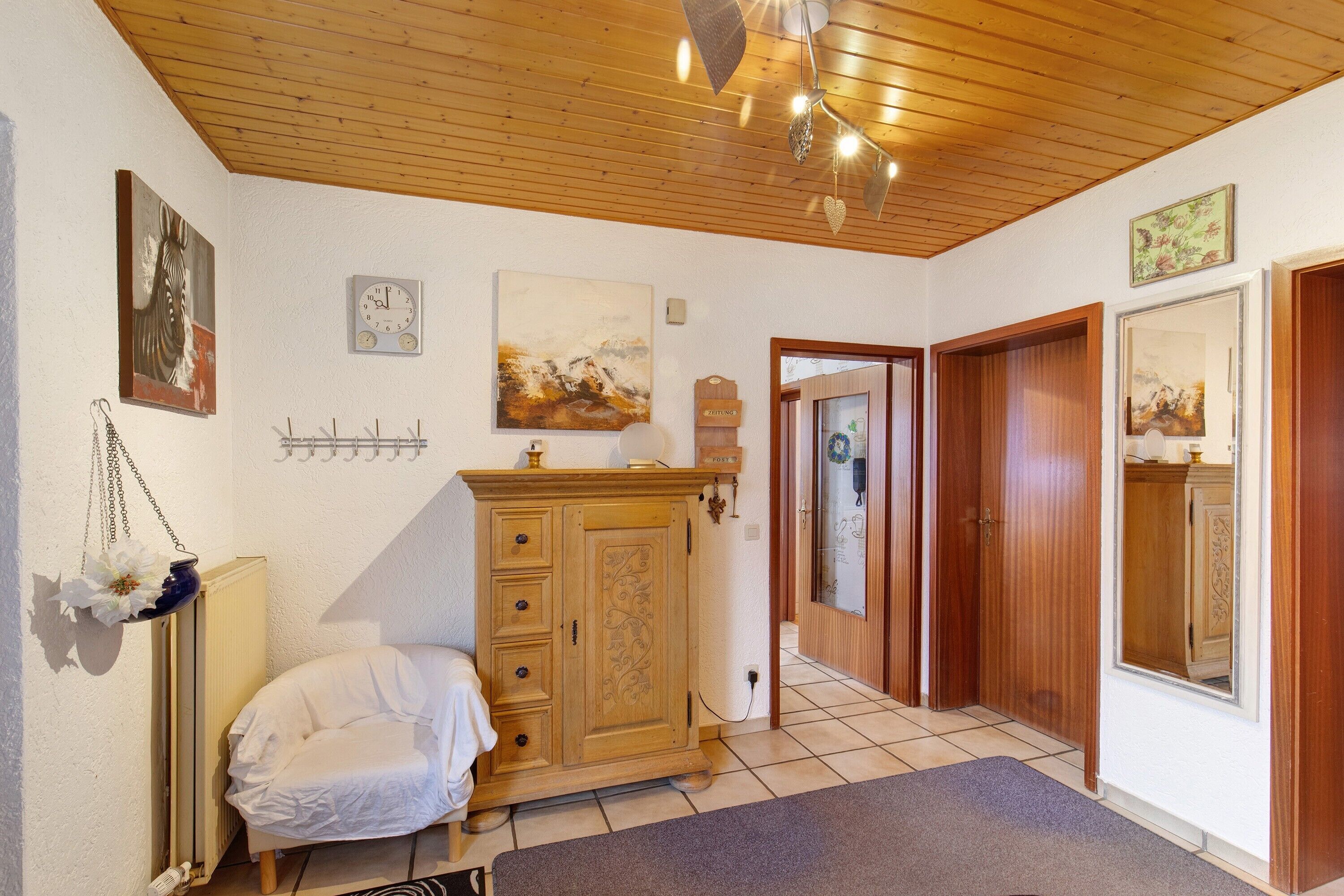 Ein Zimmer mit Holzboden, einem Bett, einem Schminktisch und einem Spiegel, sowie einer Tür zu einem anderen Raum.